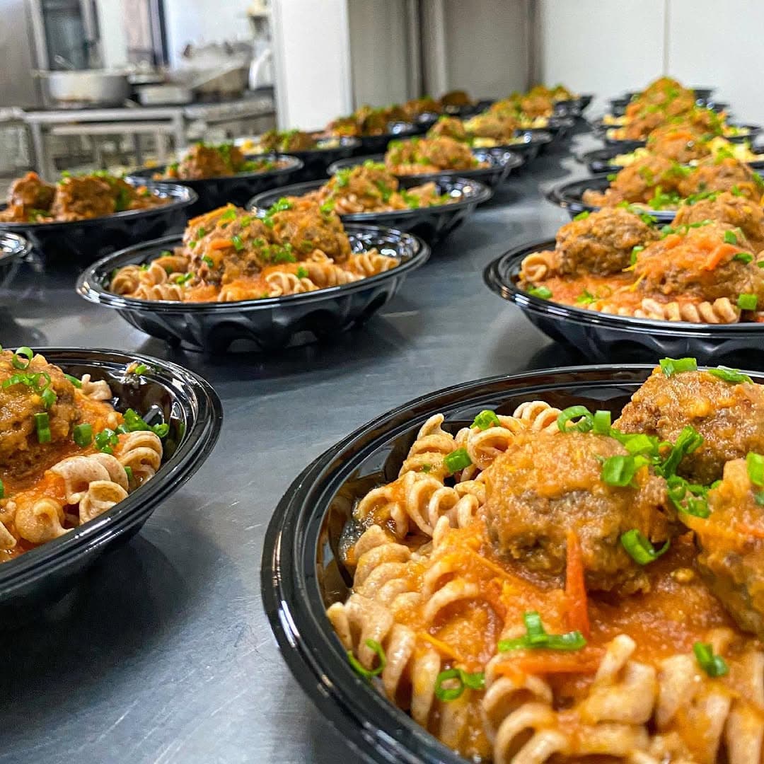 Refeições de macarrão com almôndegas em embalagens individuais, enfileiradas na bancada de inox da cozinha